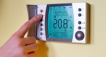 Closeup of a woman's hand setting the room temperature on a modern programmable thermostat. Save energy and money concept